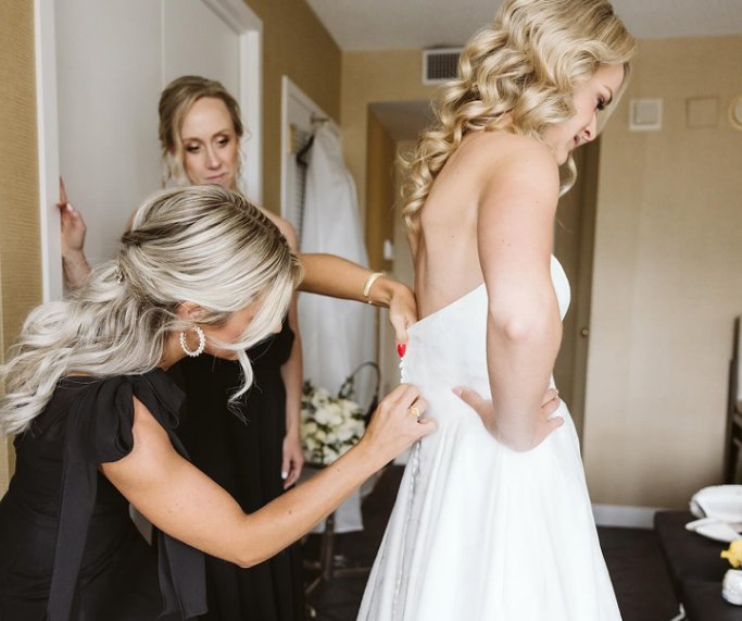 Bridesmaid helping bride with white wedding dress